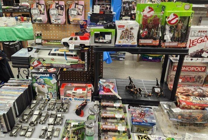 Display table packed with collectible toys, model cars, Ghostbusters, Marvel figures, and Walking Dead games.