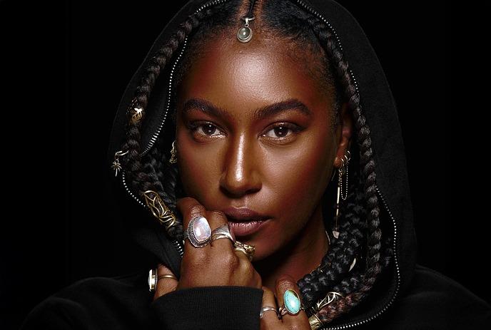 Dominique Fils-Aimé sitting cross legged in front of an audience on a dark stage.