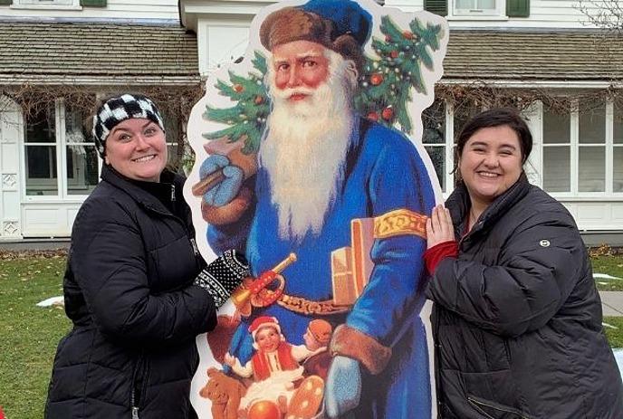 Two people standing beside a cardboard cutout of a Father Christmas with a bag of toys.