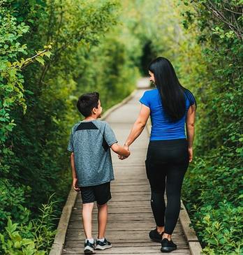 A mother and her son walking on a path into a forest