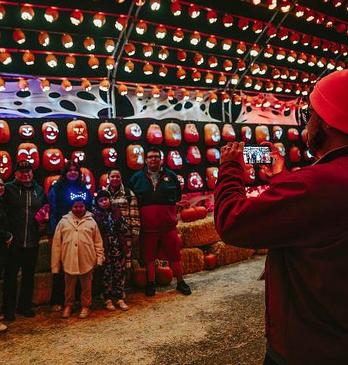 A woman with various children surrounding her near a fall display with hay and pumpkins at Clovermead Adventure Farm
