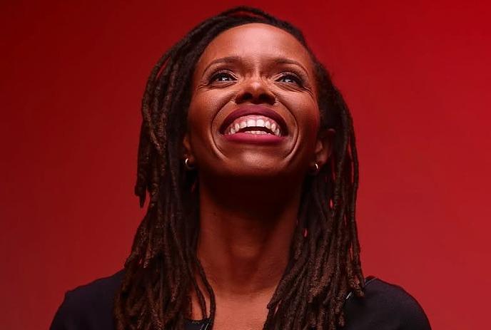 Artist smiling and looking upwards in a black dress under a red background.