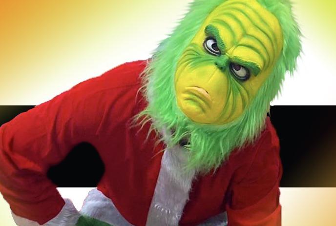 A person in a Grinch costume with a Santa jacket, white fur trim, standing playfully in a festive setting.