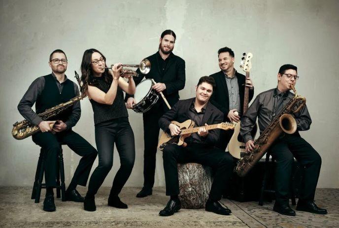 The 6 members of the André Bisson Band, posing with their instruments for the camera in a blank room, wearing formal attire.