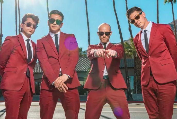 The Dreamboats wearing matching red suites and black sunglasses, posing outside on a sunny day with palm trees in the background.