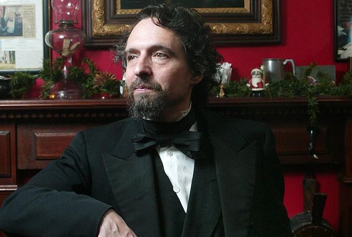 John D. Huston in a suit and bowtie sitting down, posing for the camera.