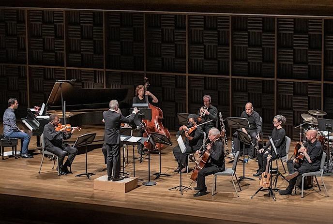 Orchestra on stage with conductor standing in front performing.