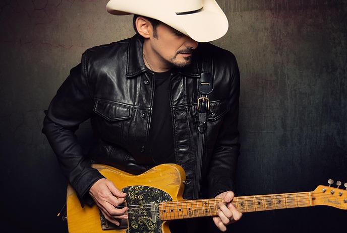 Brad Paisley wearing a cowboy hat and leather jacket, playing an electric guitar.