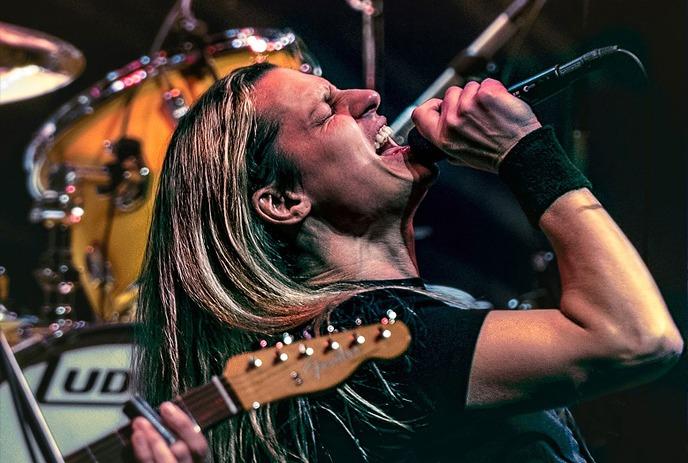 Classic Albums Live performs on stage with dramatic lighting, as the crowd raises their hands.