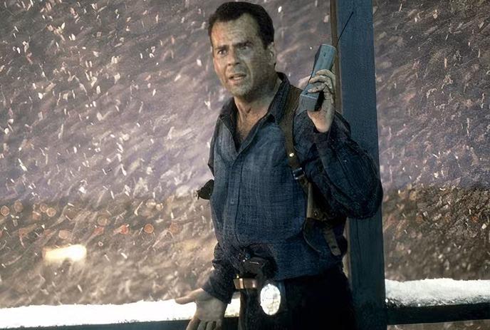 John McClane holding a phone in a snowy scene.
