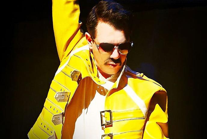 Person wearing yellow jacket and sunglasses holding a microphone singing.