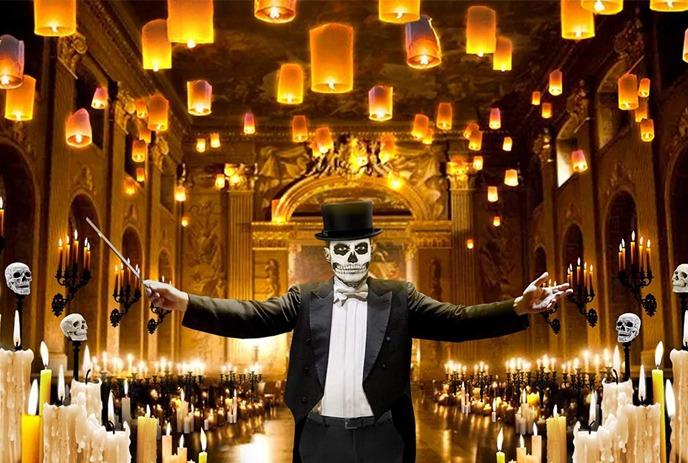 A skull-faced conductor in a tuxedo and top hat poses theatrically in a lavish, golden-lit ballroom.