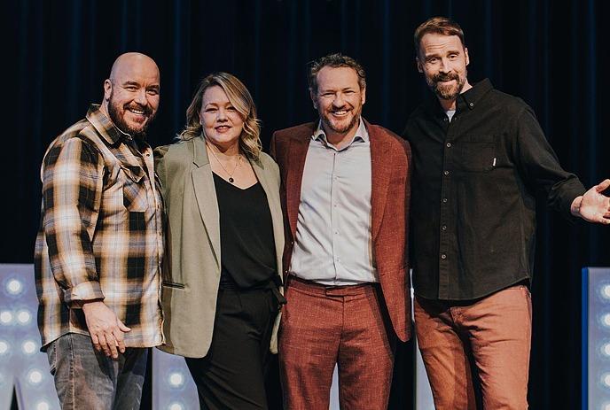 Erica Sigurdson, Pete Zedlacher, Dan Quinn and Paul Myrehaug standing on stage, smiling posing for the camera with their arms around each other.