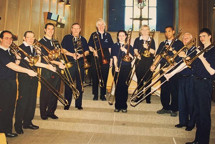Ten trombonists in navy shirts pose on steps indoors posing for a picture.