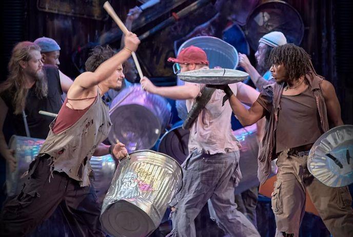 Energetic performers using trash cans and sticks as instruments in a dynamic street show.