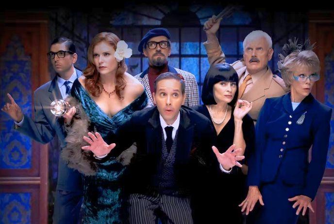 A lively group of seven people in costumes striking dramatic poses against a blue and wooden-themed backdrop.