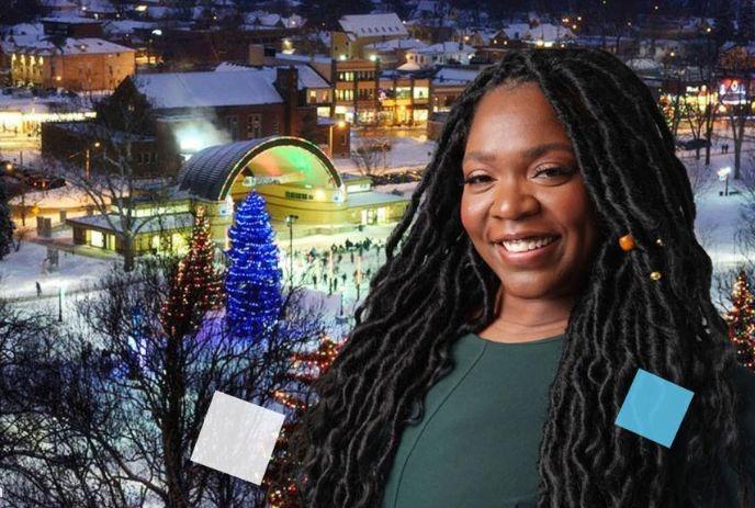 Smiling woman in front of snowy square with lit Christmas tree, festive lights and holiday crowd.