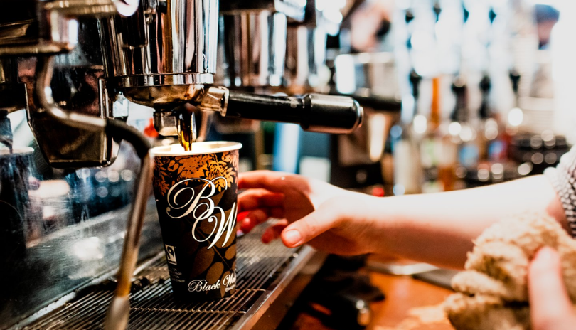 A hand grabs a fresh cup of coffee at a coffee machine.